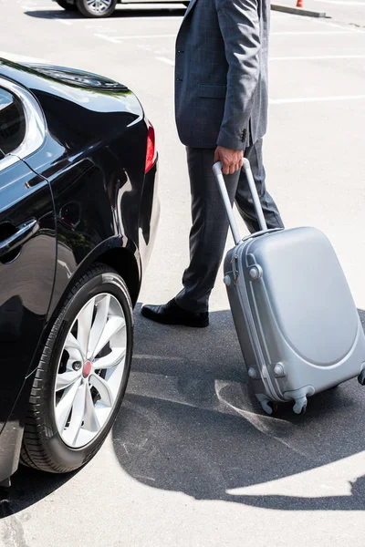 Imagen recortada de hombre de negocios que lleva el bolso de ruedas cerca del coche en la calle - foto de stock