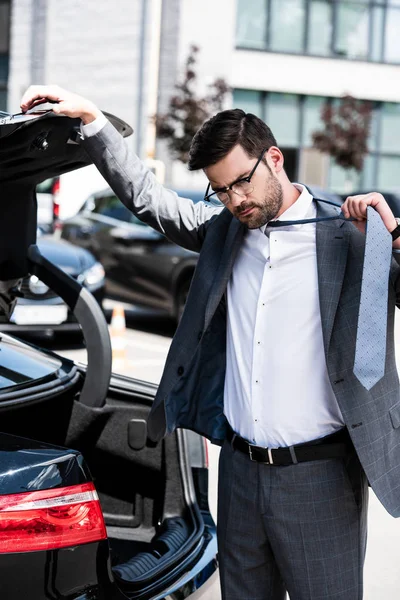 Handsome businessman closing car trunk and taking off necktie at street — Stock Photo