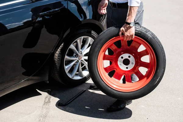 Cropped image of businessman holding tire for wheel replacement at street — Stock Photo