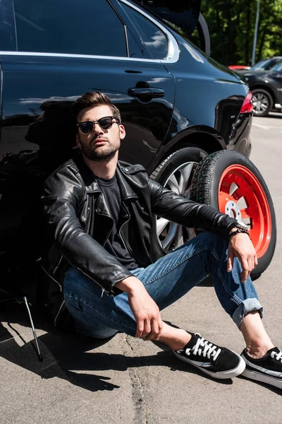 Cansado homem elegante em óculos de sol sentado perto de carro quebrado na rua — Fotografia de Stock