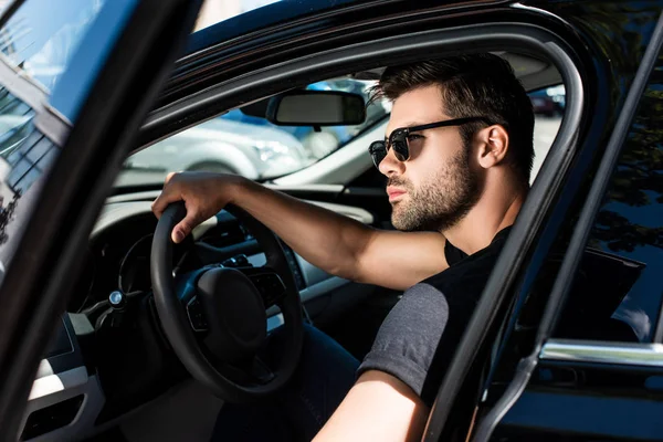 Serious stylish man in sunglasses closing door of his car at street — Stock Photo