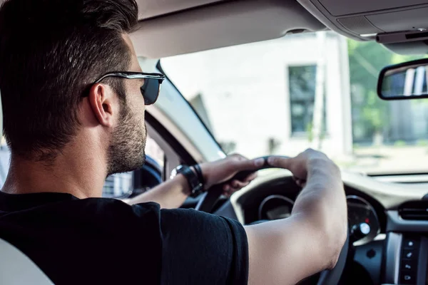 Vista posteriore di fiducioso giovane uomo elegante in occhiali da sole guida la sua auto — Foto stock