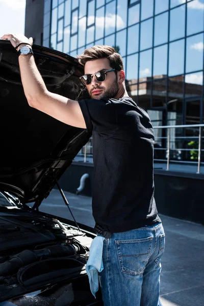 Mann mit Sonnenbrille schließt Motorhaube von Auto auf Straße — Stockfoto