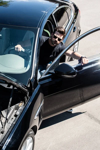 High angle view of stylish man in sunglasses going out from car with opened bonnet — Stock Photo