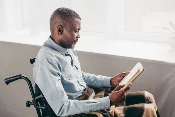 Sénior afroamericano hombre en silla de ruedas lectura libro - foto de stock