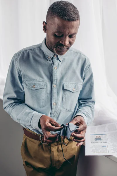 Senior african american man cleaning eyeglasses with cloth at home — Stock Photo