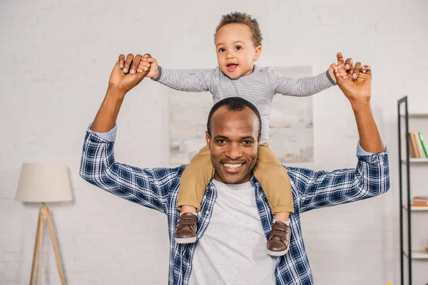 Glücklicher junger Vater trägt entzückenden kleinen Sohn am Hals und lächelt in die Kamera — Stockfoto