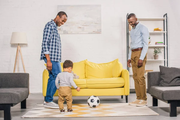 Счастливый африканский американский отец, дедушка и маленький сын играют в футбол дома — стоковое фото