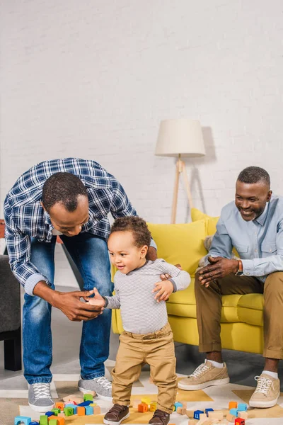 Happy senior man looking at young man helping little son walking at home — Stock Photo
