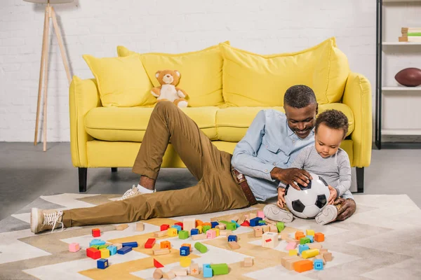 Abuelo feliz y pequeño nieto jugando con la pelota de fútbol en casa - foto de stock