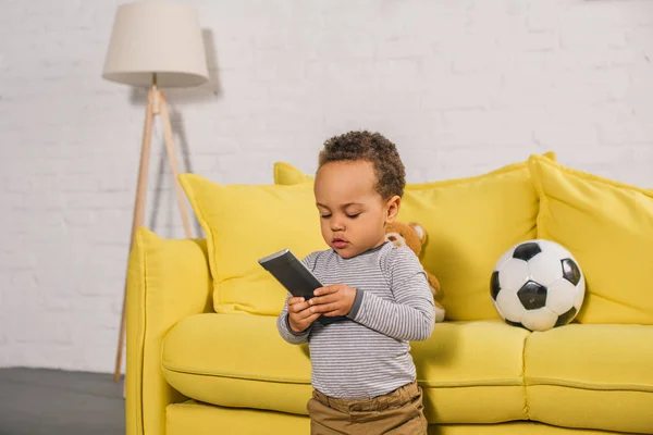 Adorable little african american child holding remote controller at home — Stock Photo