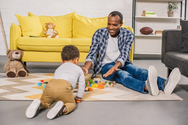 Glücklicher afrikanisch-amerikanischer Vater und kleiner Sohn spielen zu Hause mit bunten Blöcken — Stockfoto