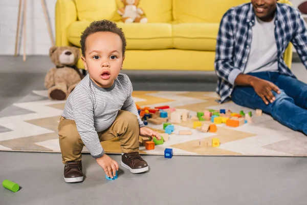 Adorável afro-americano criança olhando para a câmera enquanto brincava com o pai em casa — Fotografia de Stock