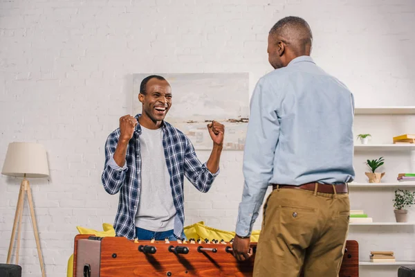 Senior father and smiling adult son playing table football at home — Stock Photo