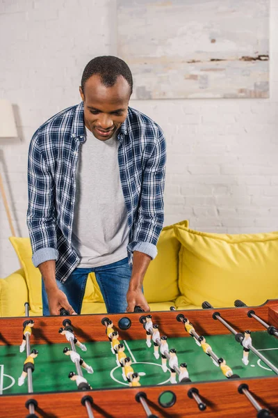 Sorridente giovane uomo africano americano che gioca a calcio balilla a casa — Foto stock