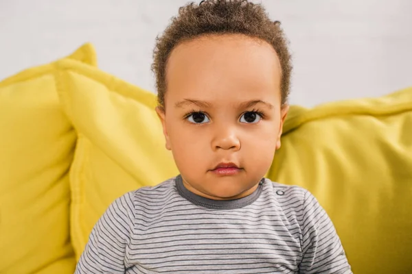Nahaufnahme Porträt eines entzückenden afrikanisch-amerikanischen Kleinkindes, das auf einer gelben Couch in die Kamera blickt — Stockfoto