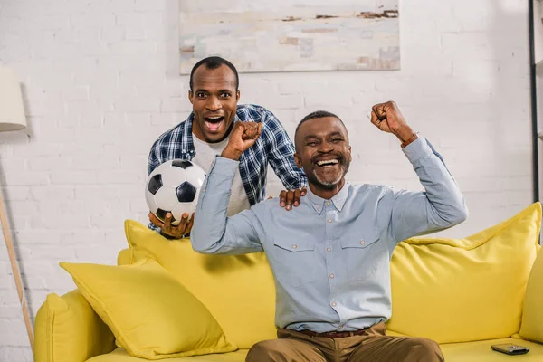 Emocionado padre e hijo con pelota de fútbol triunfando y sonriendo a la cámara - foto de stock