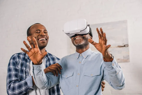 Sonriente joven mirando feliz padre mayor usando auriculares de realidad virtual — Stock Photo