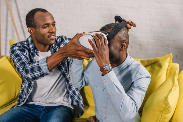 Jovem sorridente vestindo fone de ouvido realidade virtual para pai sênior — Fotografia de Stock