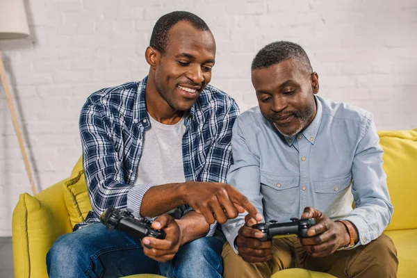 Felice padre afroamericano e figlio adulto utilizzando joystick insieme a casa — Foto stock