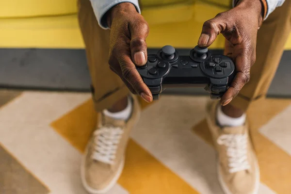 Cropped shot of african american man sitting on sofa and playing with joystick — Stock Photo