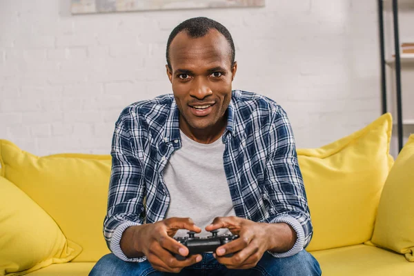 Young african american man playing with joystick and smiling at camera — Stock Photo
