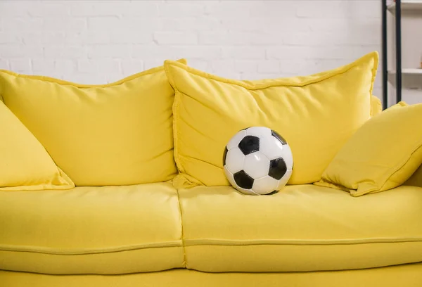 Pallone da calcio su divano giallo in camera accogliente — Foto stock