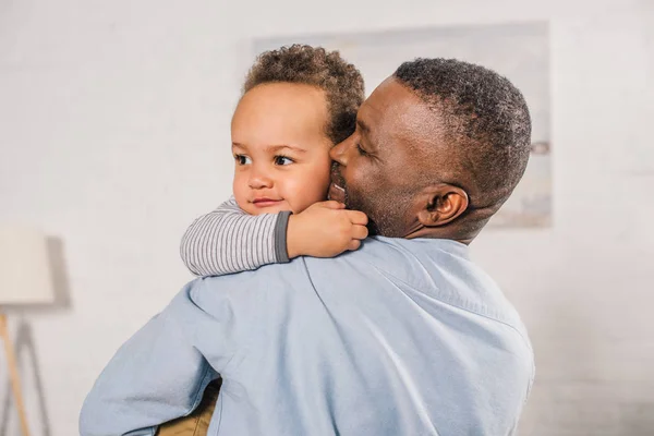 Feliz africano americano abuelo abrazando adorable poco nieto en casa - foto de stock