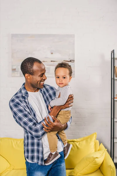 Feliz joven padre llevando adorable pequeño hijo en casa - foto de stock