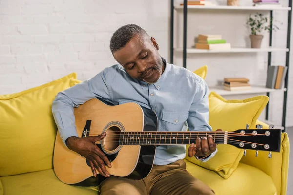 Sorridente uomo africano americano che suona la chitarra acustica a casa — Foto stock