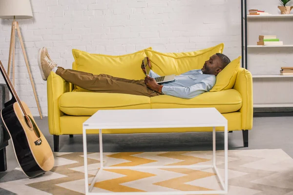 Anziano uomo africano americano sdraiato sul divano e utilizzando il computer portatile — Foto stock
