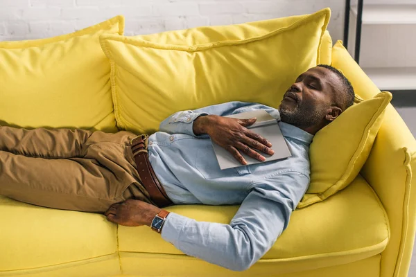 Vue grand angle de l'homme afro-américain sénior dormant avec livre sur canapé — Photo de stock