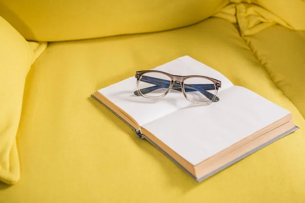 Крупный план очков и книга с пустыми страницами на желтом диване — стоковое фото