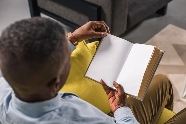 Високий кут зору старший афроамериканський чоловік читає книгу вдома — стокове фото