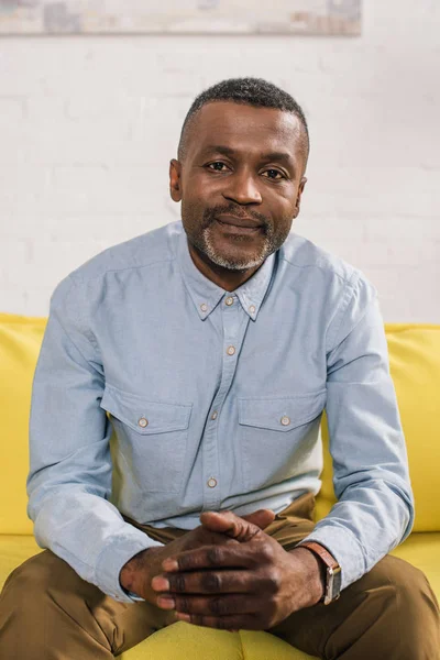 Senior homme afro-américain assis sur le canapé et regardant la caméra — Photo de stock