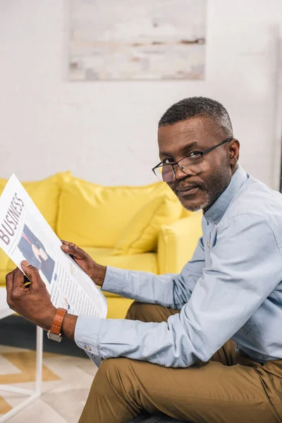 Hombre afroamericano de alto nivel con anteojos sosteniendo periódico y mirando la cámara - foto de stock