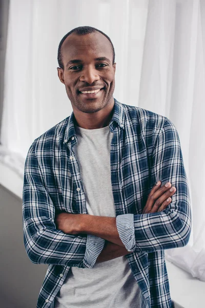 Handsome young african american man standing with crossed arms and smiling at camera — Stock Photo