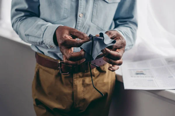 Cropped shot of senior african american man cleaning eyeglasses with cloth — Stock Photo