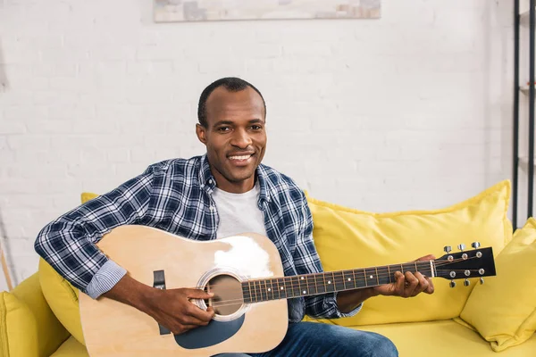 Bonito afro-americano homem tocando guitarra acústica e sorrindo para a câmera — Fotografia de Stock