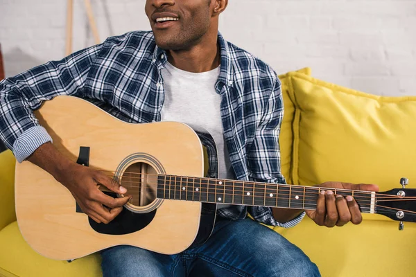 Cortado tiro de sorrir afro-americano homem tocando guitarra acústica em casa — Fotografia de Stock