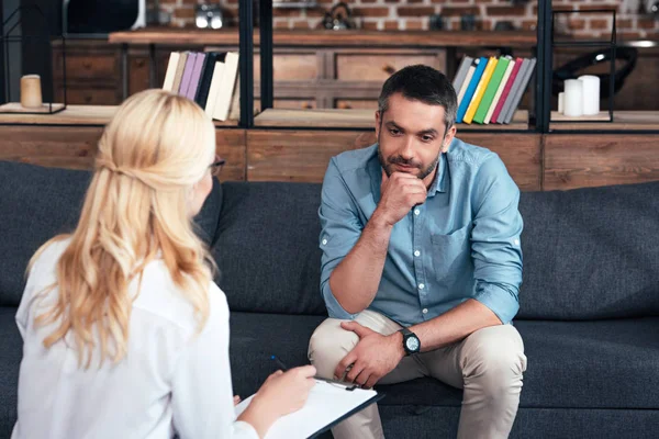 Rückansicht einer weiblichen Beraterin, die im Klemmbrett schreibt und mit einem männlichen Patienten im Büro spricht — Stockfoto