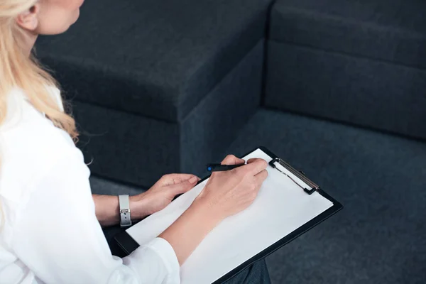 Imagen recortada de la mujer consejera escribiendo en portapapeles vacío durante la sesión de terapia en la oficina - foto de stock