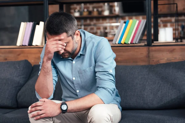 Depressed man with hand on forehead sitting on sofa in psychiatrist office — Stock Photo