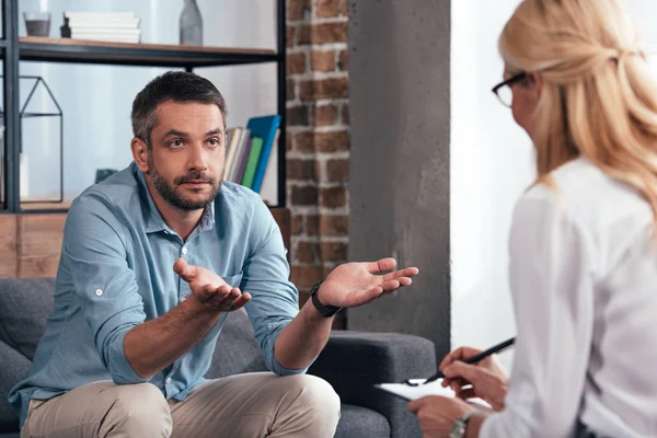 Uomo maturo con braccia larghe che parla con psichiatra femminile nel suo ufficio — Foto stock