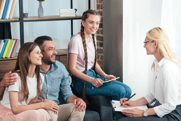 Female counselor writing in clipboard on therapy session of family with daughter in office — Stock Photo