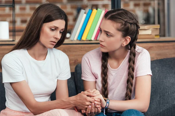 Selective focus of teenage girl holding hands of frustrated mother on sofa — Stock Photo