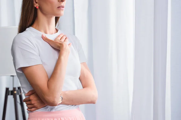 Abgeschnittenes Bild einer besorgten Frau mit der Hand auf der Brust vor Vorhängen zu Hause — Stockfoto