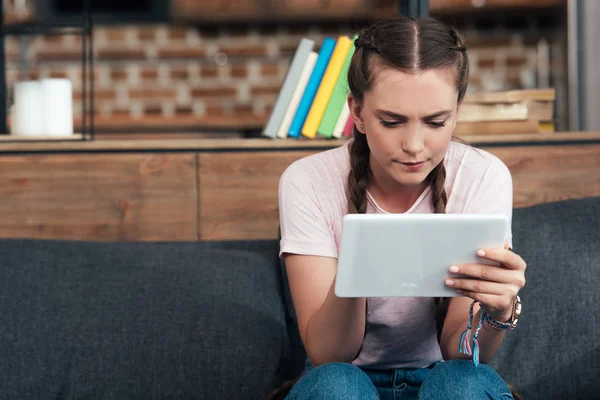 Adolescente concentrado usando tablet digital enquanto sentado no sofá em casa — Fotografia de Stock