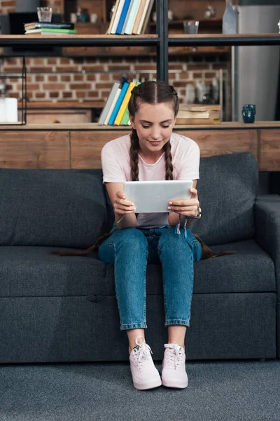 Adolescent souriant utilisant une tablette numérique tout en étant assis sur le canapé à la maison — Photo de stock