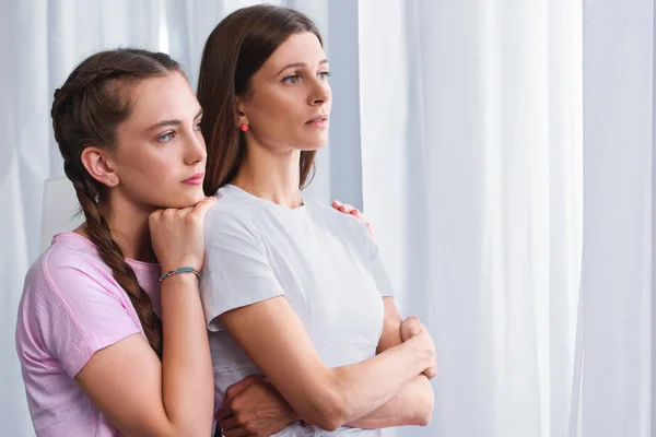 Vista laterale della figlia abbracciando la madre preoccupata da dietro a casa — Foto stock